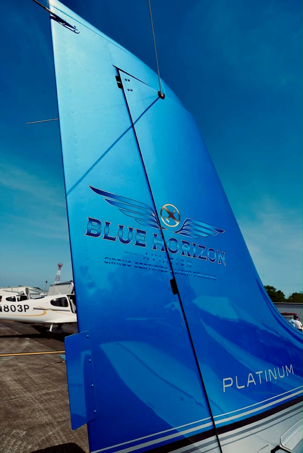The Blue Horizon Aviation winged mark and wordmark in pale blue on the deep blue tail of one of the school’s Cirrus aircraft, with another of their aircraft parked behind
